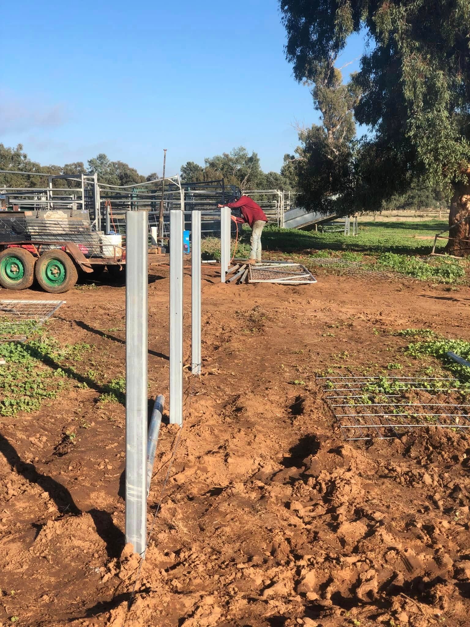A man is working on a fence in a dirt field.