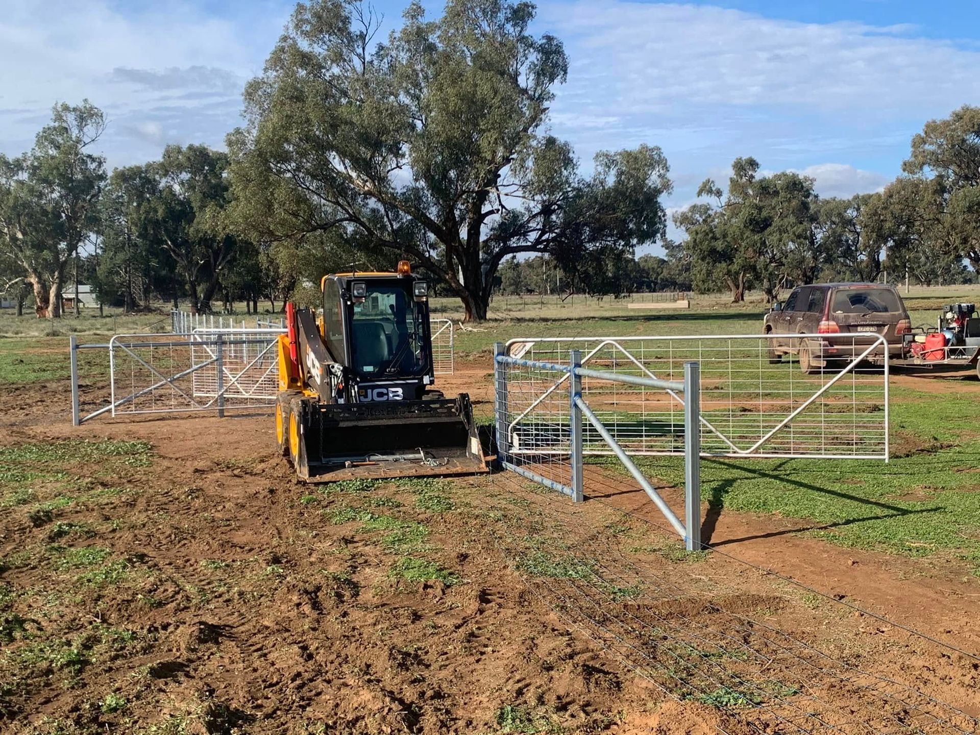 A bulldozer is driving through a dirt field next to a gate.
