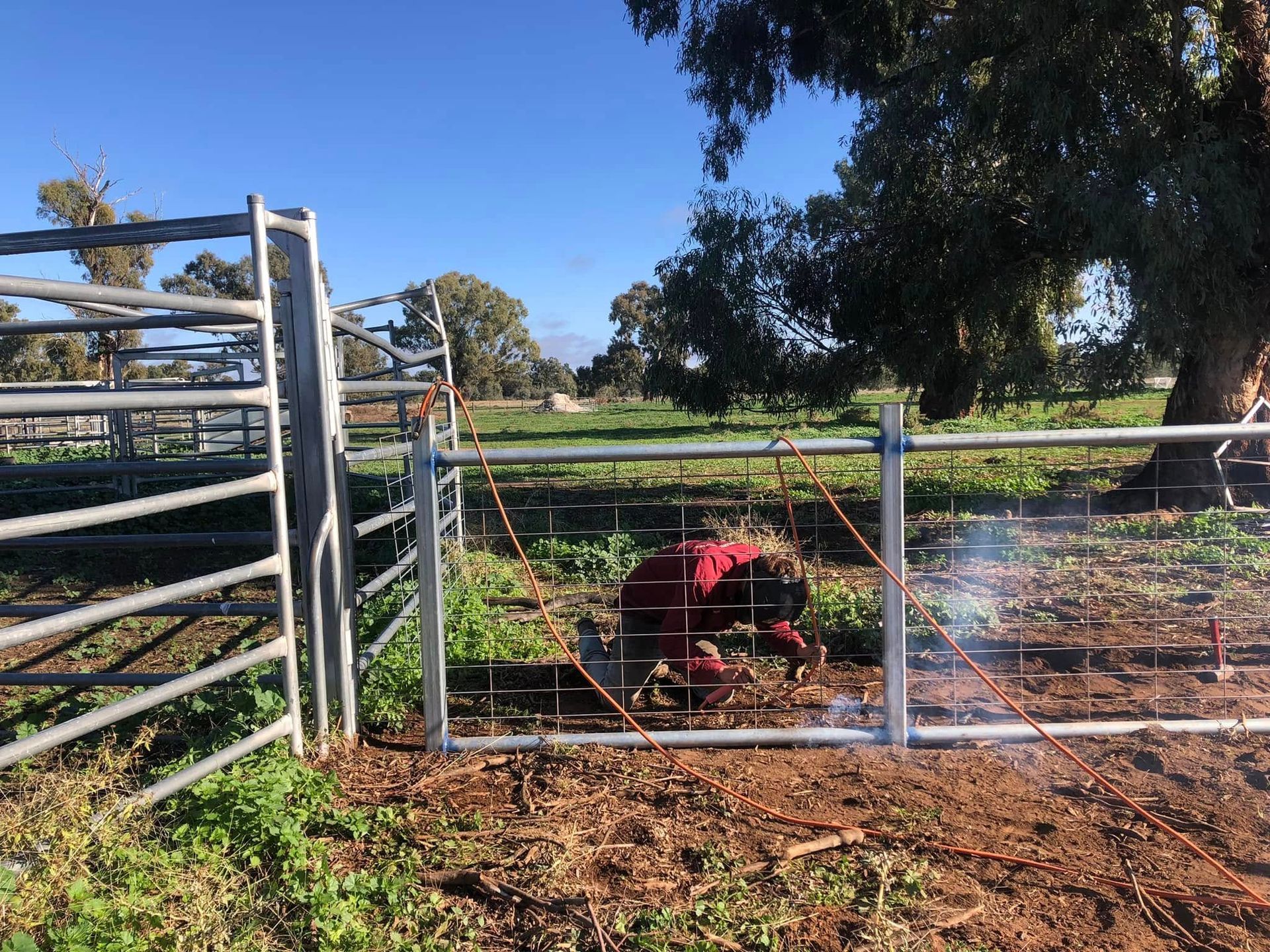 A man is welding a metal fence in a field.