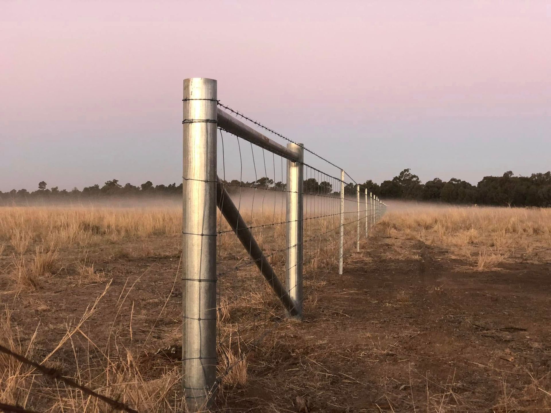 A fence in a field with a pink sky in the background