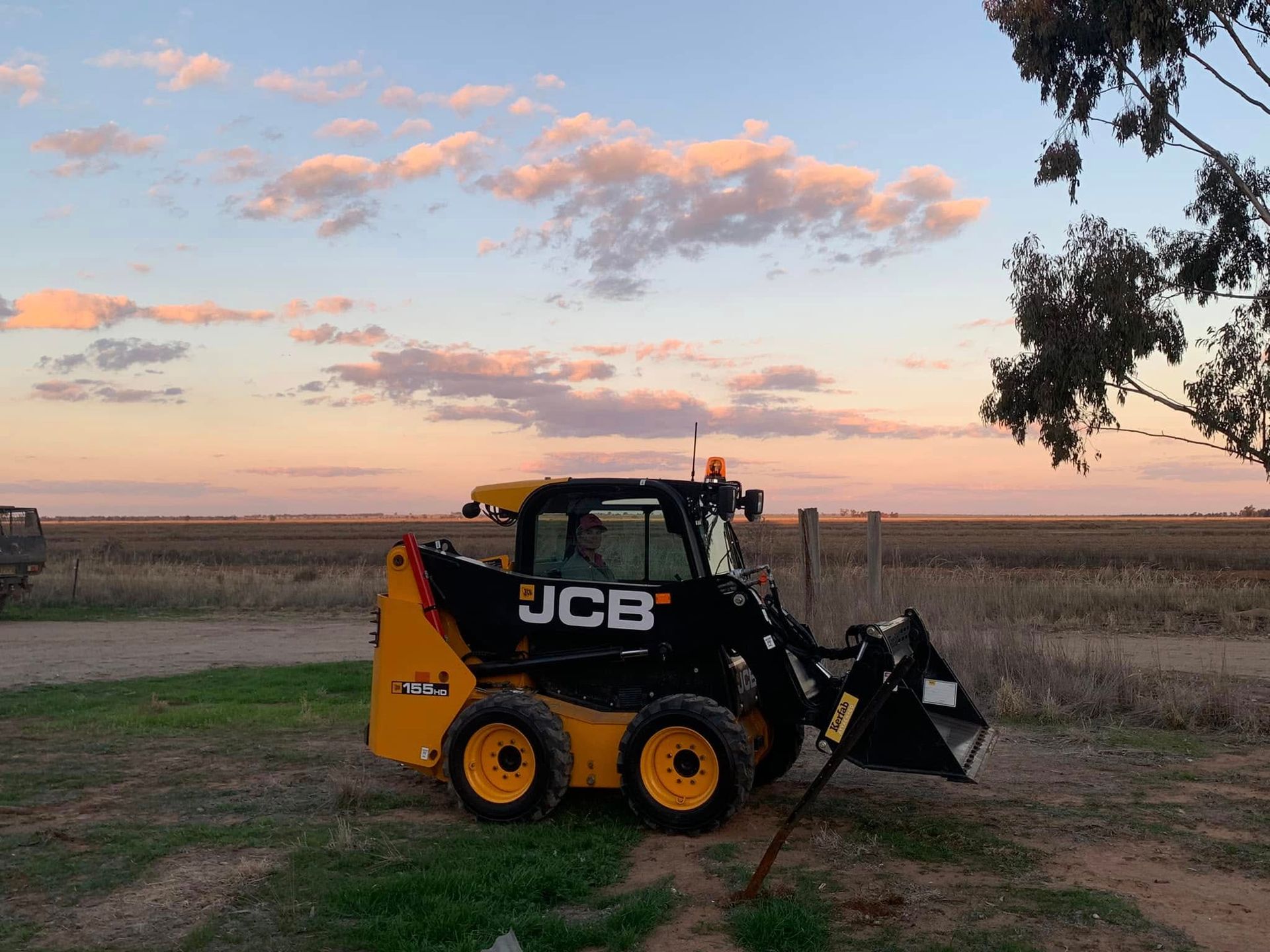 A jcb skid steer is parked in a field at sunset.
