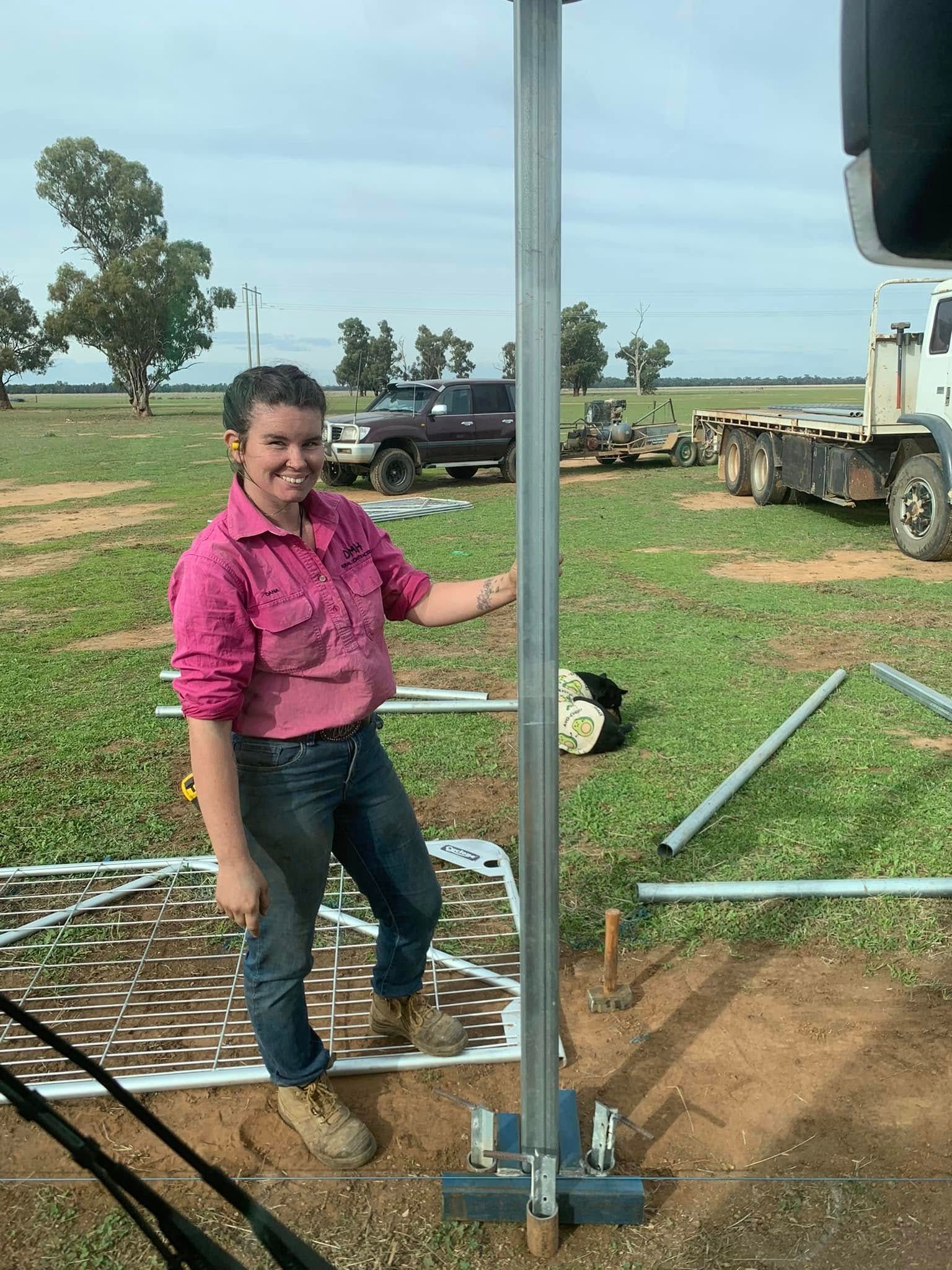 A woman in a pink shirt is standing next to a pole in a field.