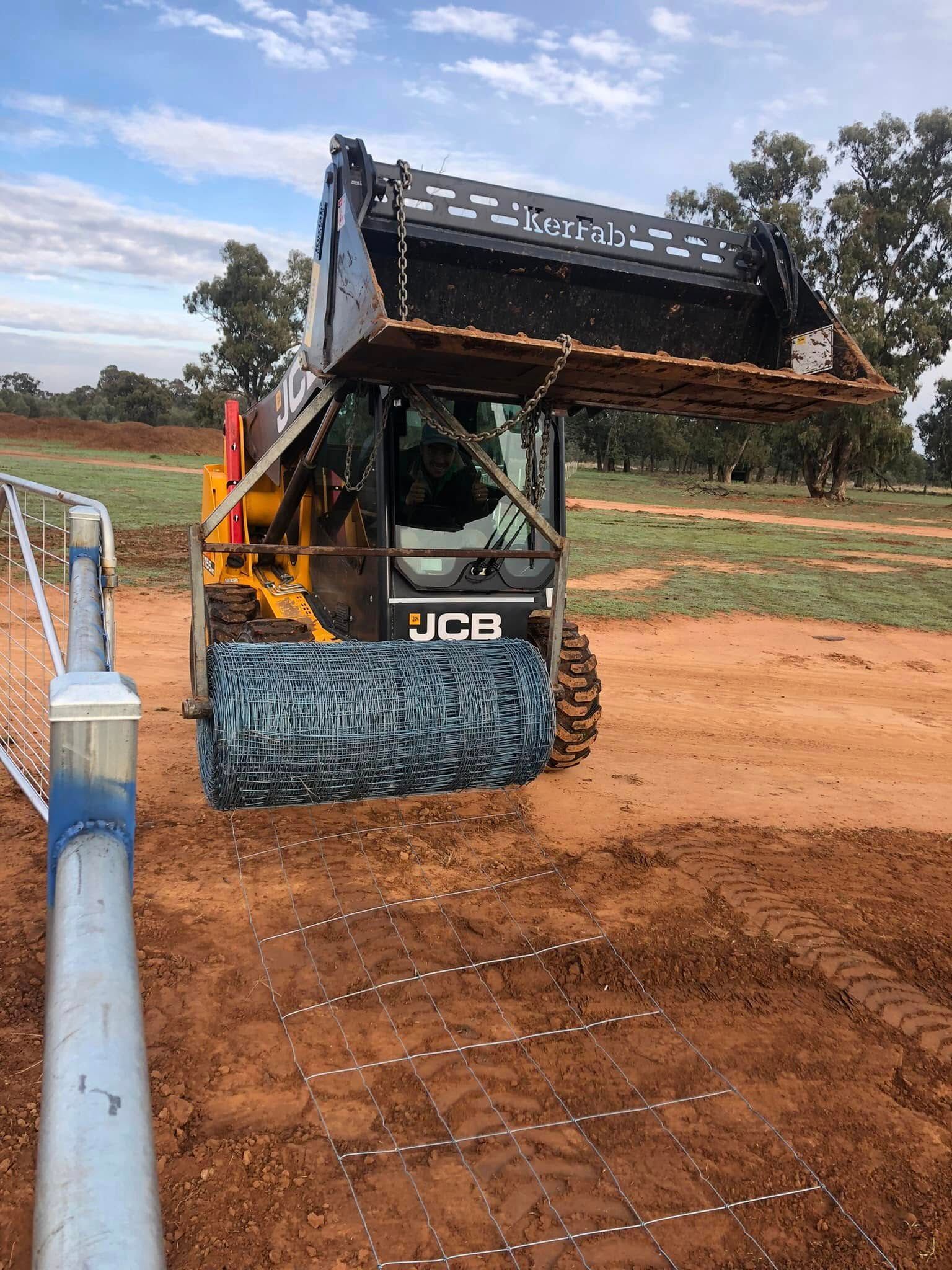 A bulldozer is moving dirt in a field next to a fence.