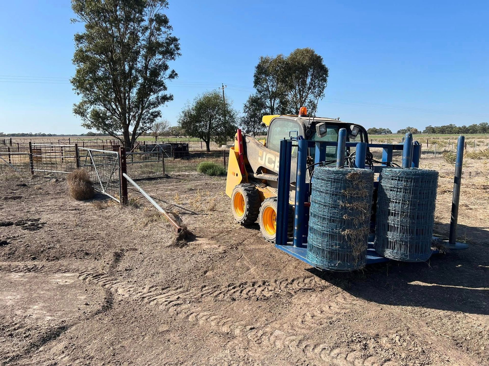 A yellow and blue tractor is parked in a dirt field.