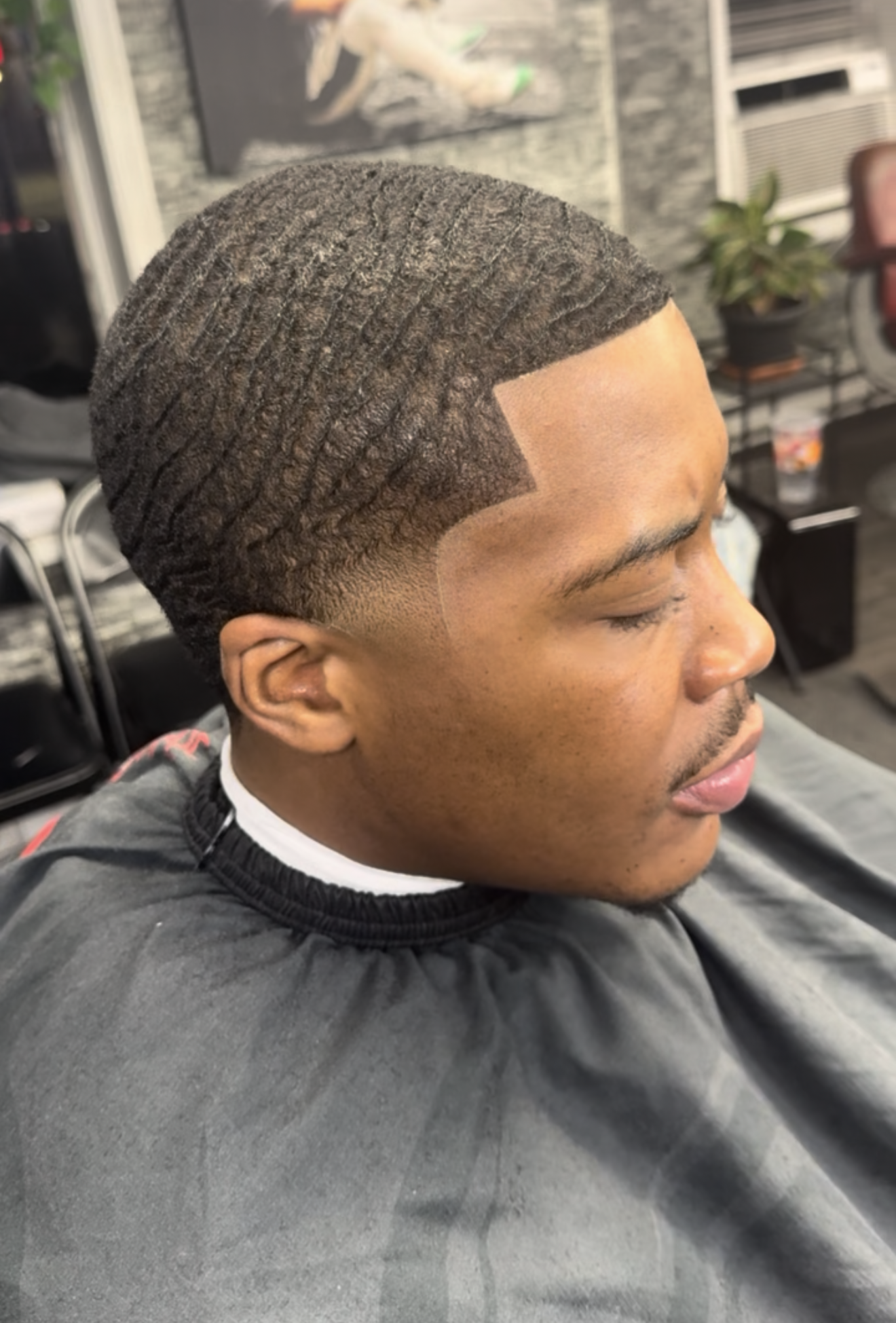 Man with a wavy haircut, a line-up, wearing a barber cape. In a barber shop.