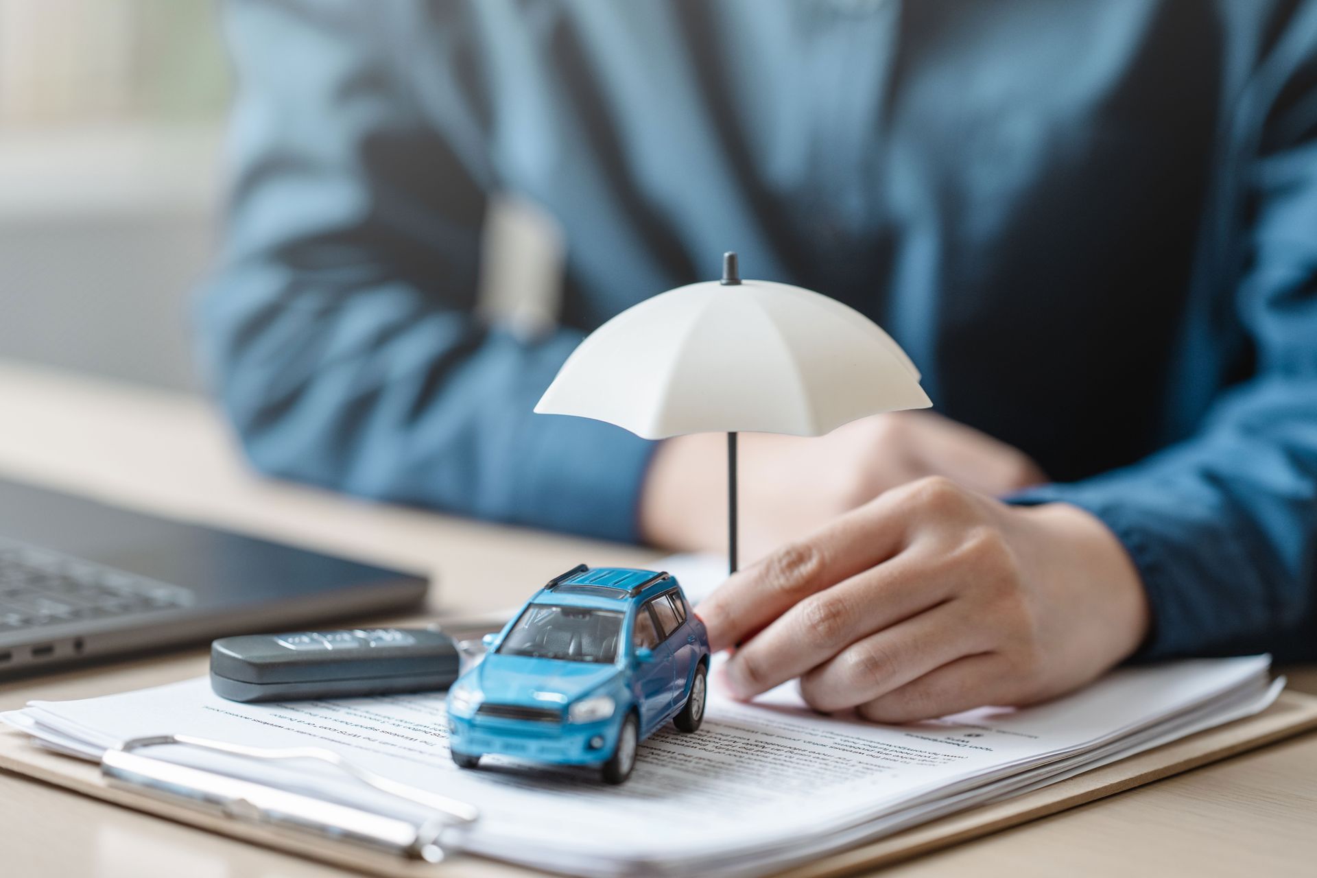 Car insurance concept with blue toy car, umbrella, and documents on desk for vehicle protection.