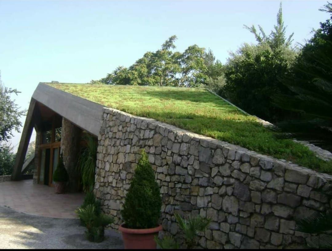 Edificio con tetto verde, muro in pietra e alberi sullo sfondo.