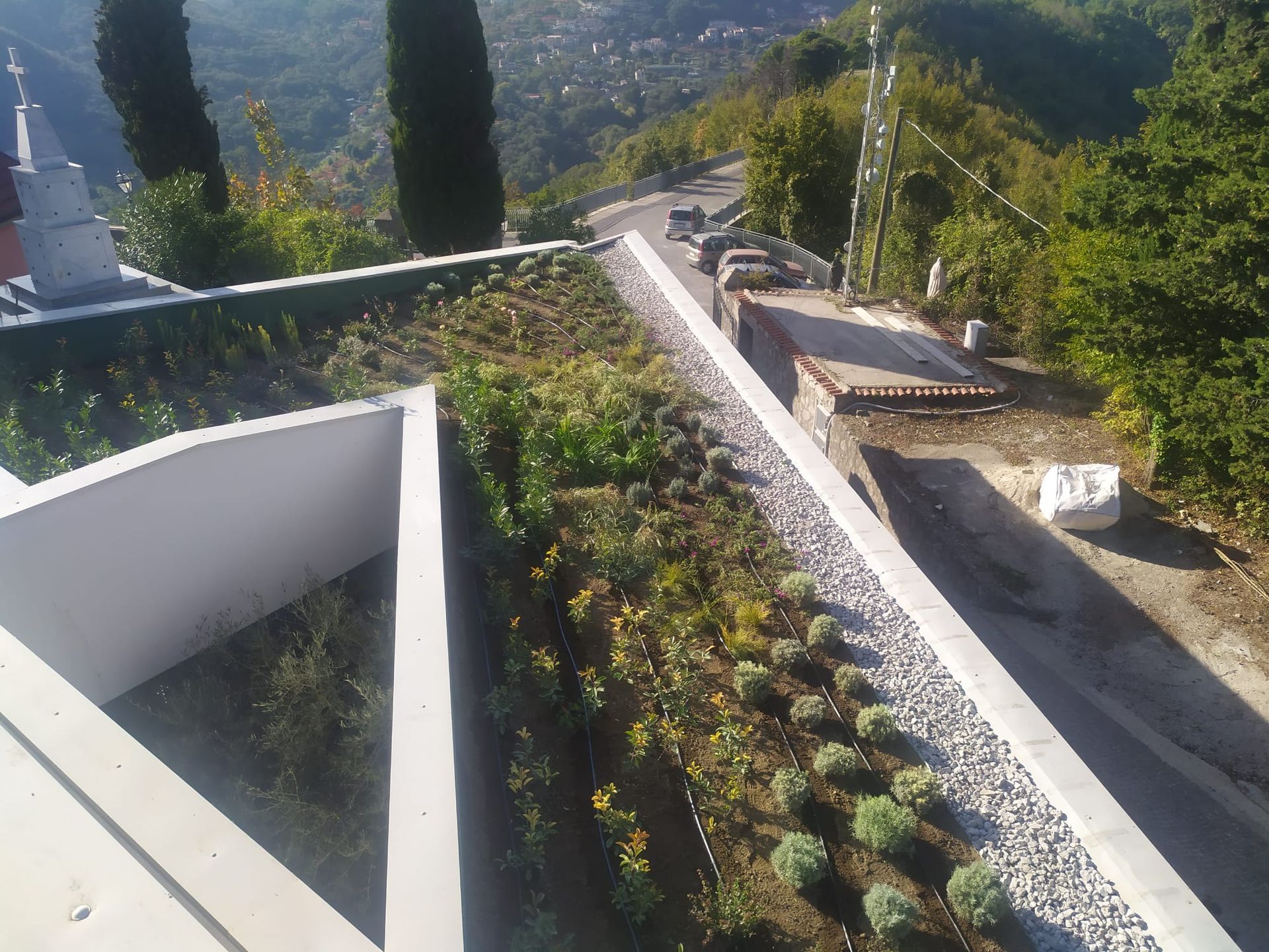 Tetto verde con piante lungo una strada in collina; pareti in cemento bianco.