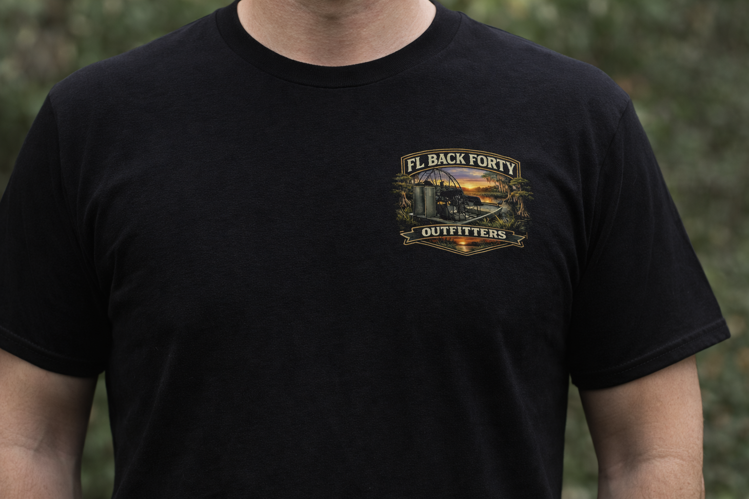 Black t-shirt with front and back designs. Front shows logo. Back has a person observing a swamp scene, with text.