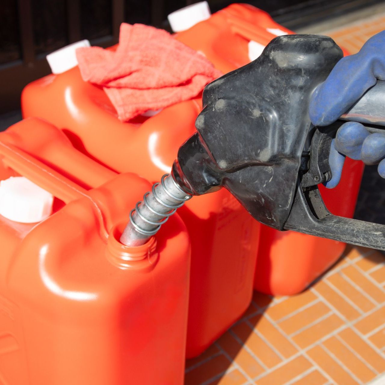 A person is pumping gas into an orange container.