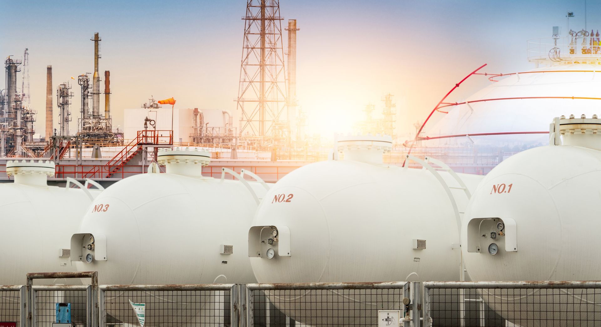 A row of white tanks sitting next to each other in front of a oil refinery.