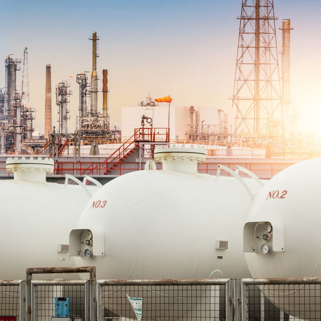 A row of white tanks sitting next to each other in front of a oil refinery.