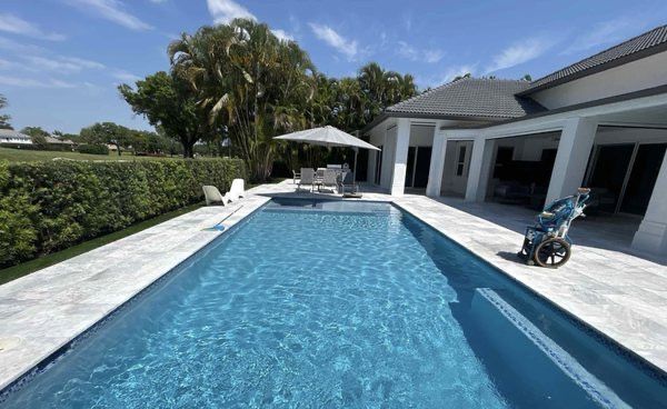 Backyard pool with blue water, white patio, umbrella, and golf cart beside a modern house