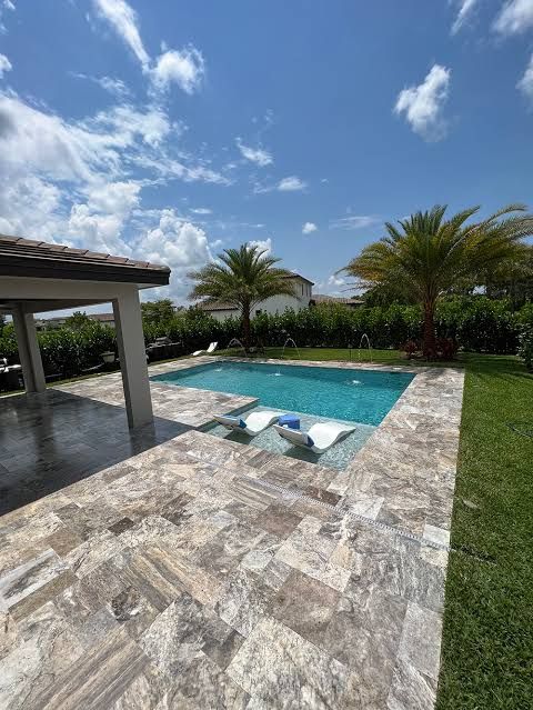 Modern backyard patio with a small blue pool, lounge chairs, palm trees, and a bright sky