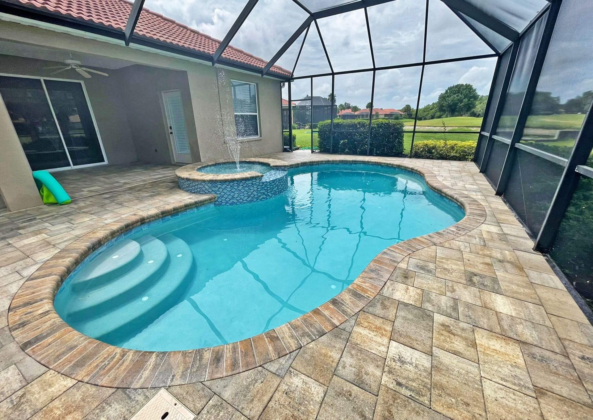 Screened backyard pool with turquoise water, stone deck, and patio beside a house