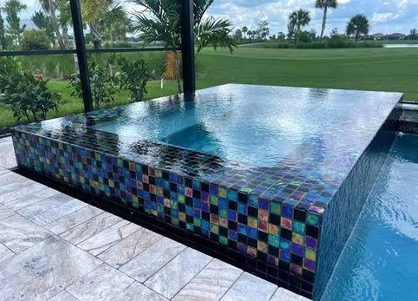 Modern tiled pool with raised edge and blue water beside a grassy golf course.