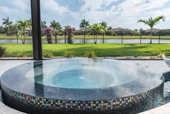 Round tiled hot tub on a patio overlooking a grassy yard and palm trees near a lake