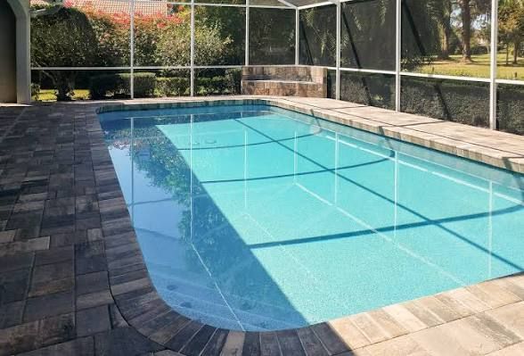 Blue rectangular swimming pool in a screened backyard patio with stone coping and tiled deck