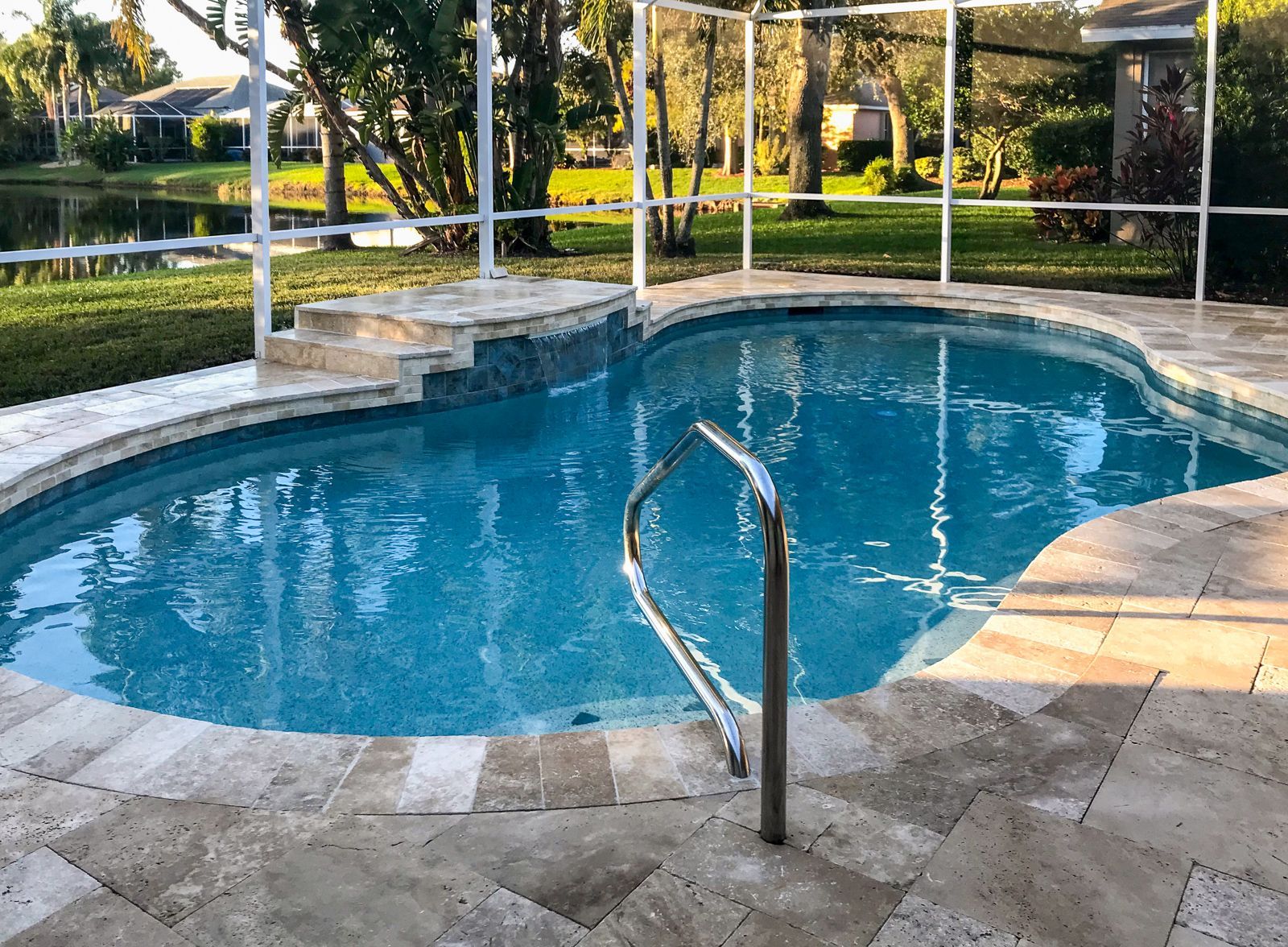 Backyard pool with stone deck, metal handrail, and screened enclosure in sunlight