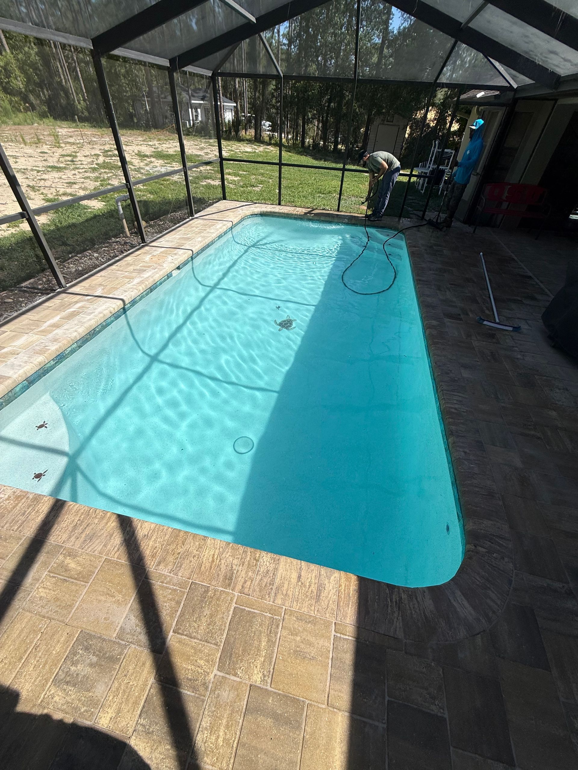 Covered backyard pool with clear blue water beside a wooden deck and fence sides.