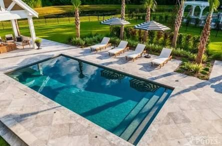 Luxurious backyard pool with lounge chairs, palm trees, and a covered patio overlooking manicured lawns