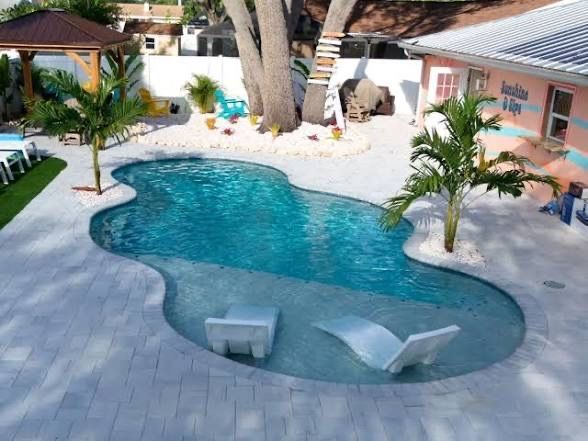 Tropical backyard pool with white deck, palm trees, lounge chairs, and a gazebo