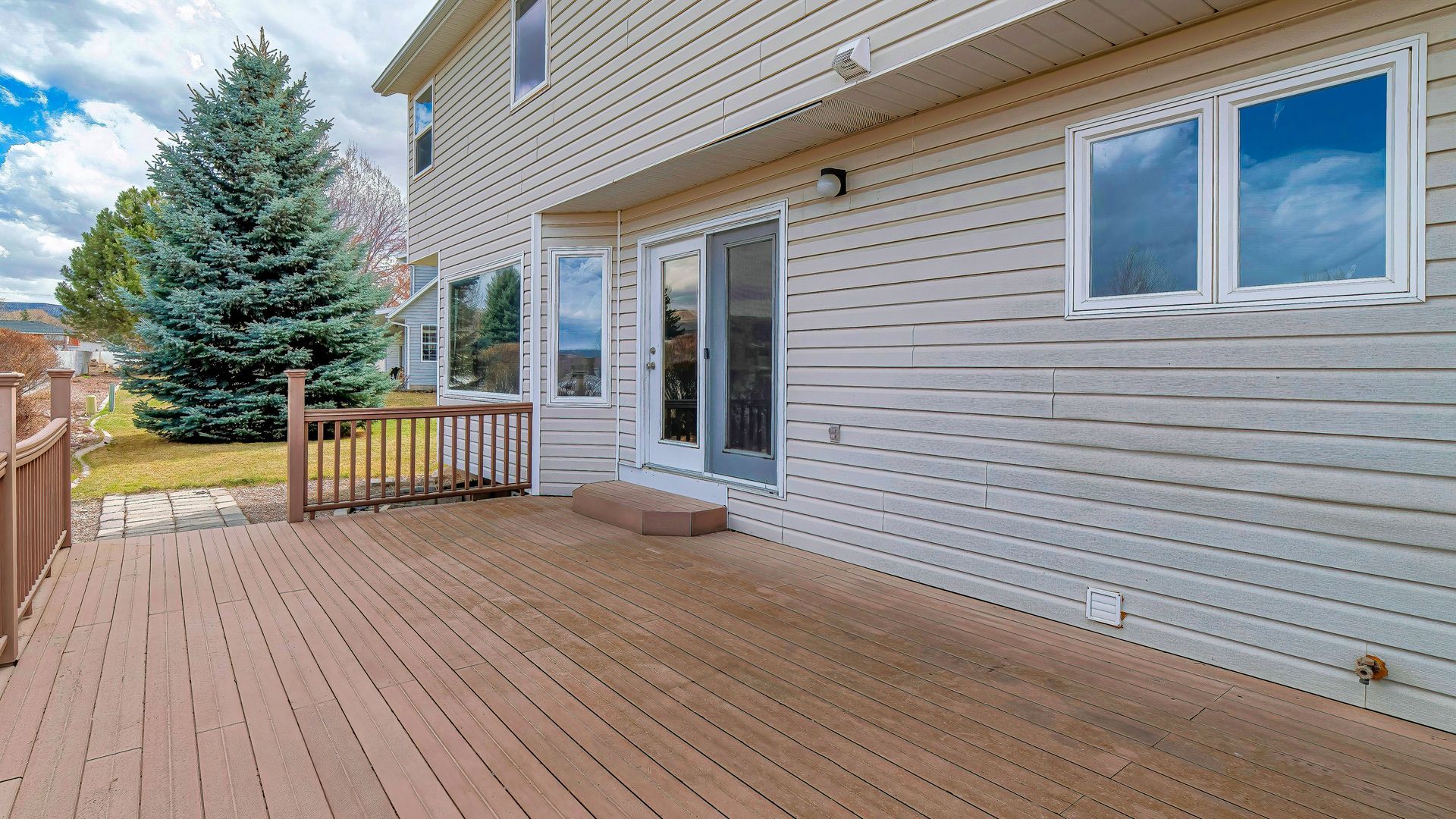 Wooden backyard deck beside a beige house with sliding glass doors and a fenced yard.