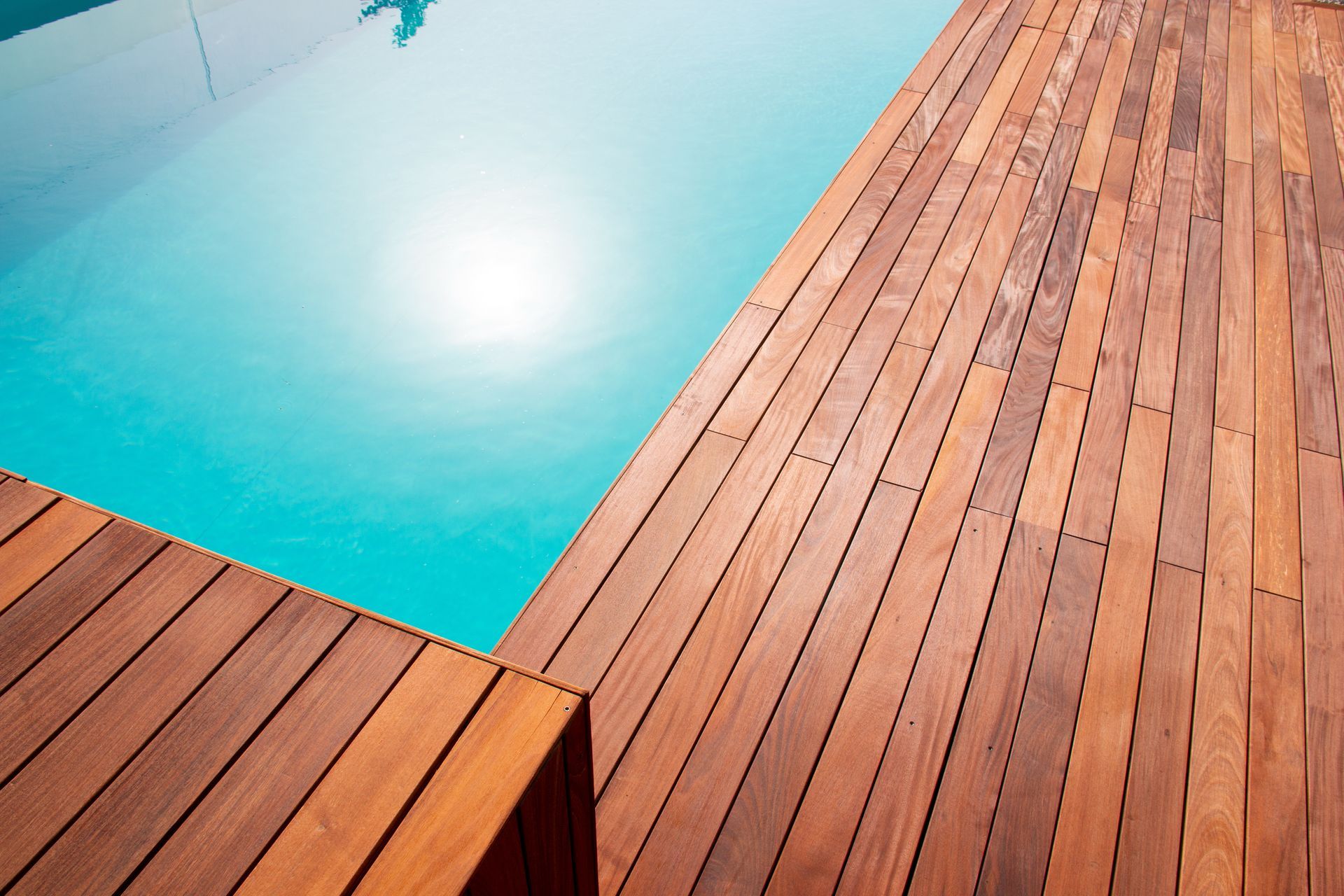 Turquoise pool beside a sunlit wooden deck with diagonal planks