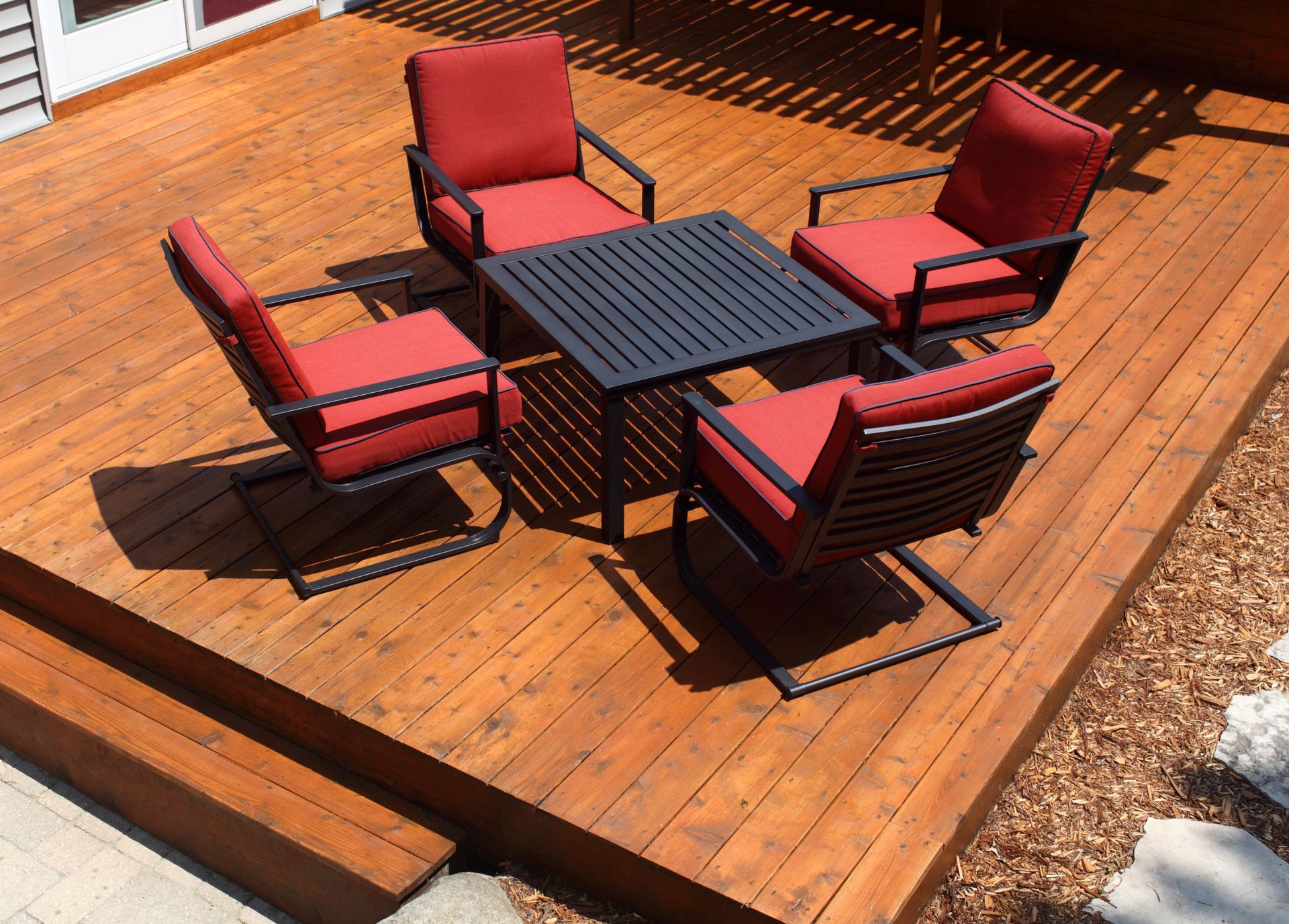 Red cushioned patio chairs around a square black table on a wooden deck