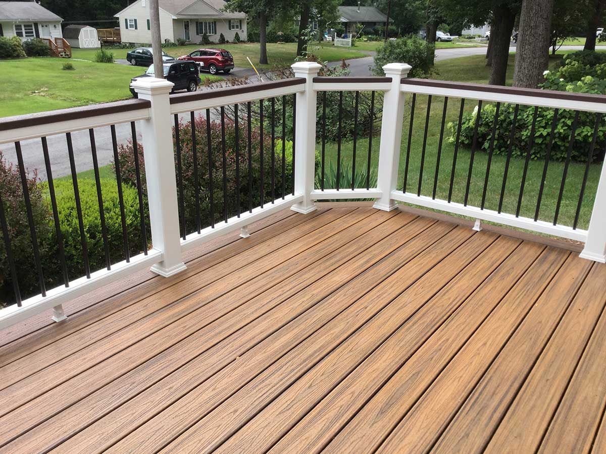 Wooden deck with white railing and black metal balusters overlooking a suburban front yard and street.