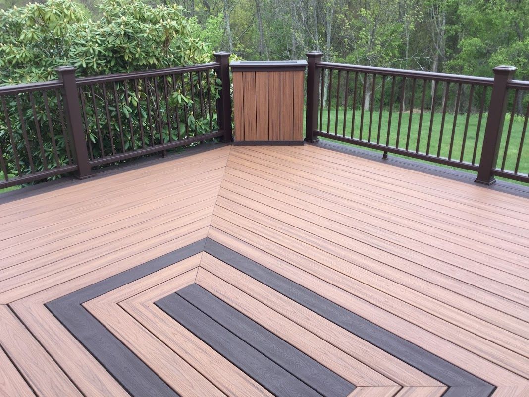 Wooden deck with dark railing and a small gate, surrounded by green trees and shrubs.