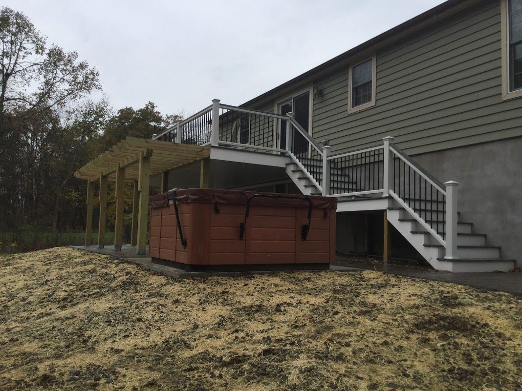 Elevated house with gray siding, white stairs, and a large brown hot tub on a wooden deck.