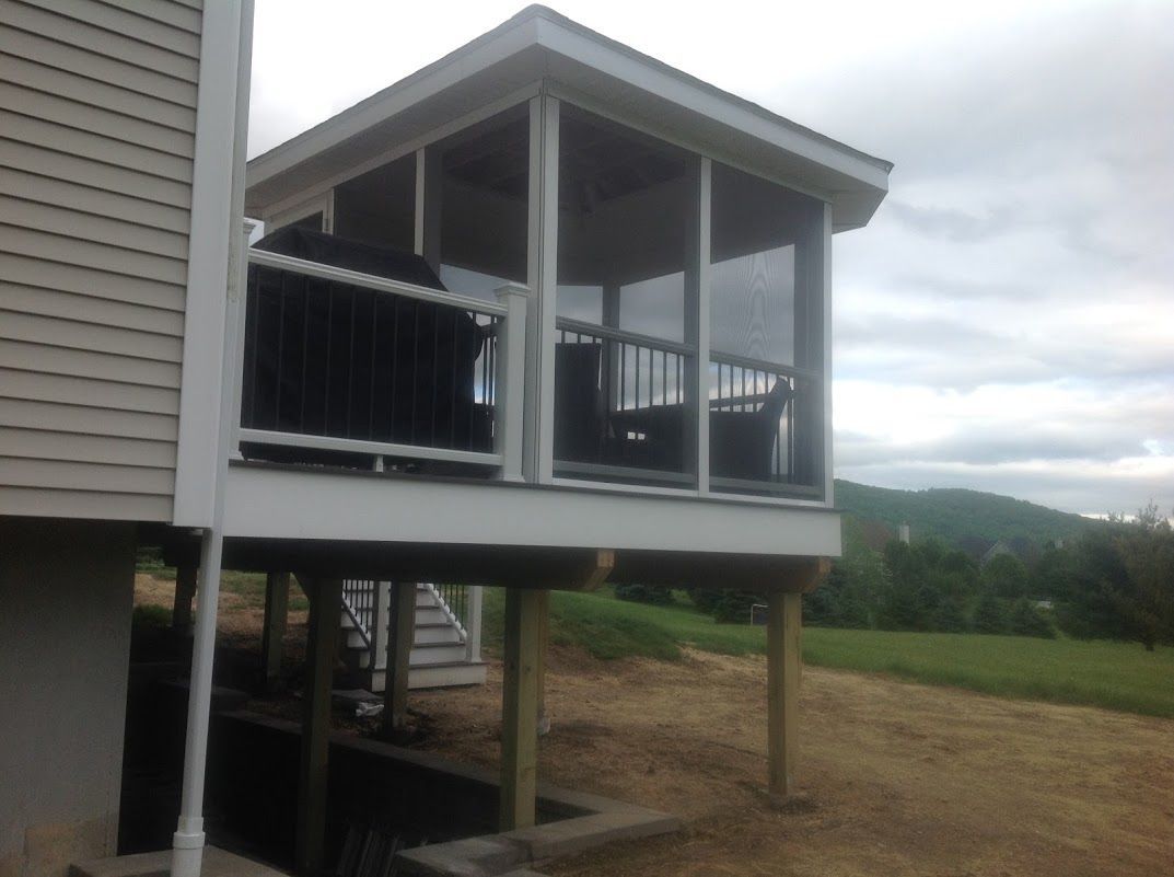 Covered porch on stilts beside a house, overlooking a grassy hillside under cloudy skies.