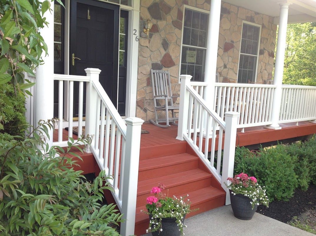 Front porch with red steps, white railings, stone wall, and potted flowers by the entrance