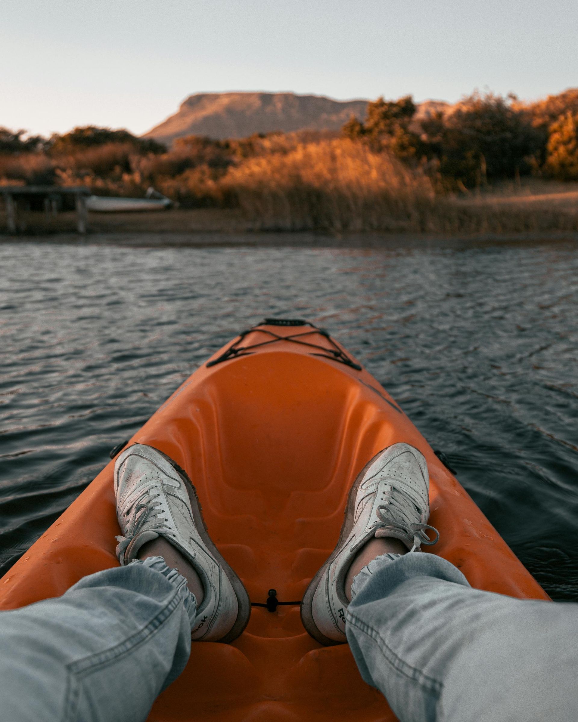Person in orange kayak on water, feet visible, mountain in background.