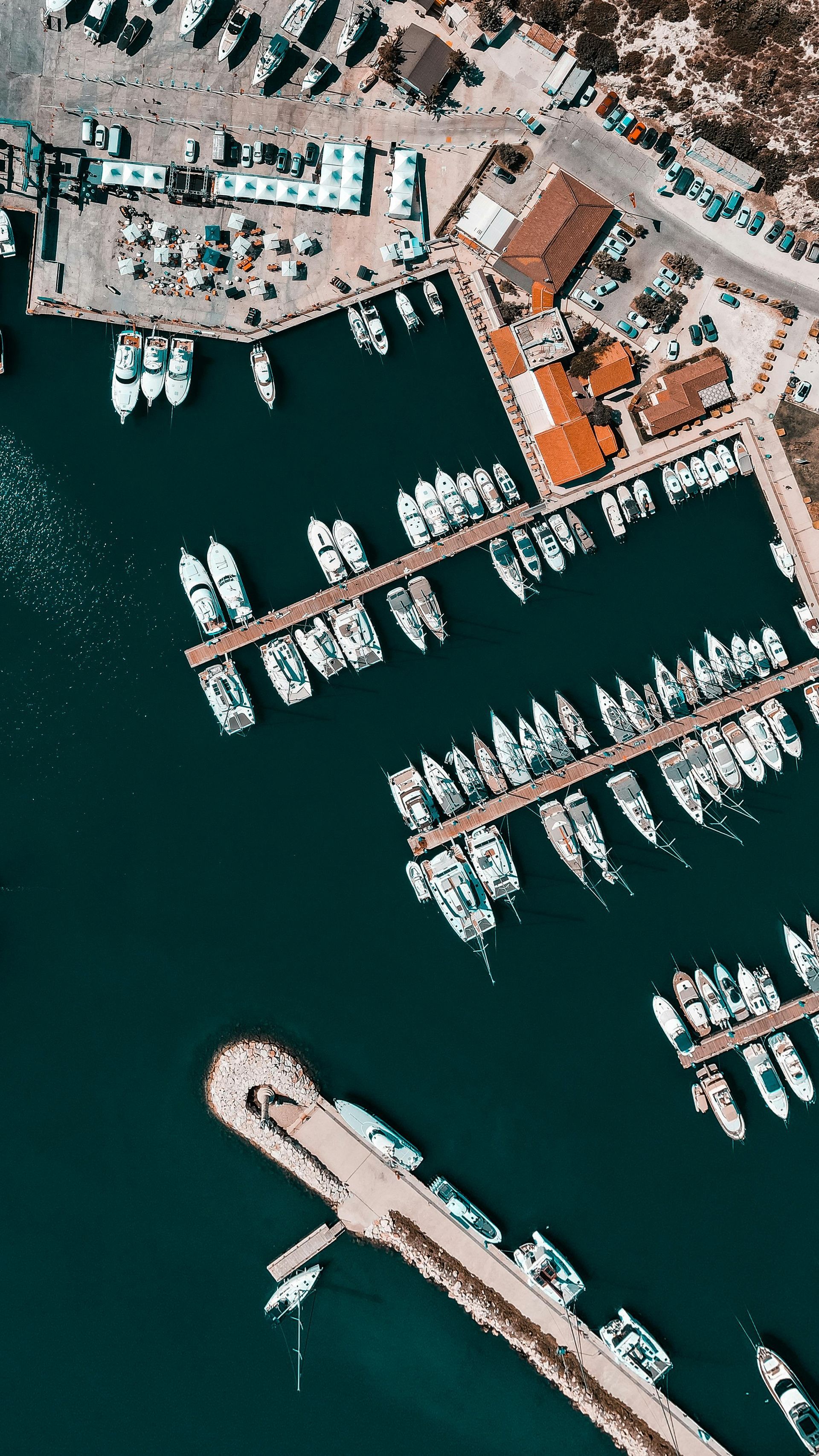 Aerial view of a marina filled with white boats docked along piers in turquoise water.
