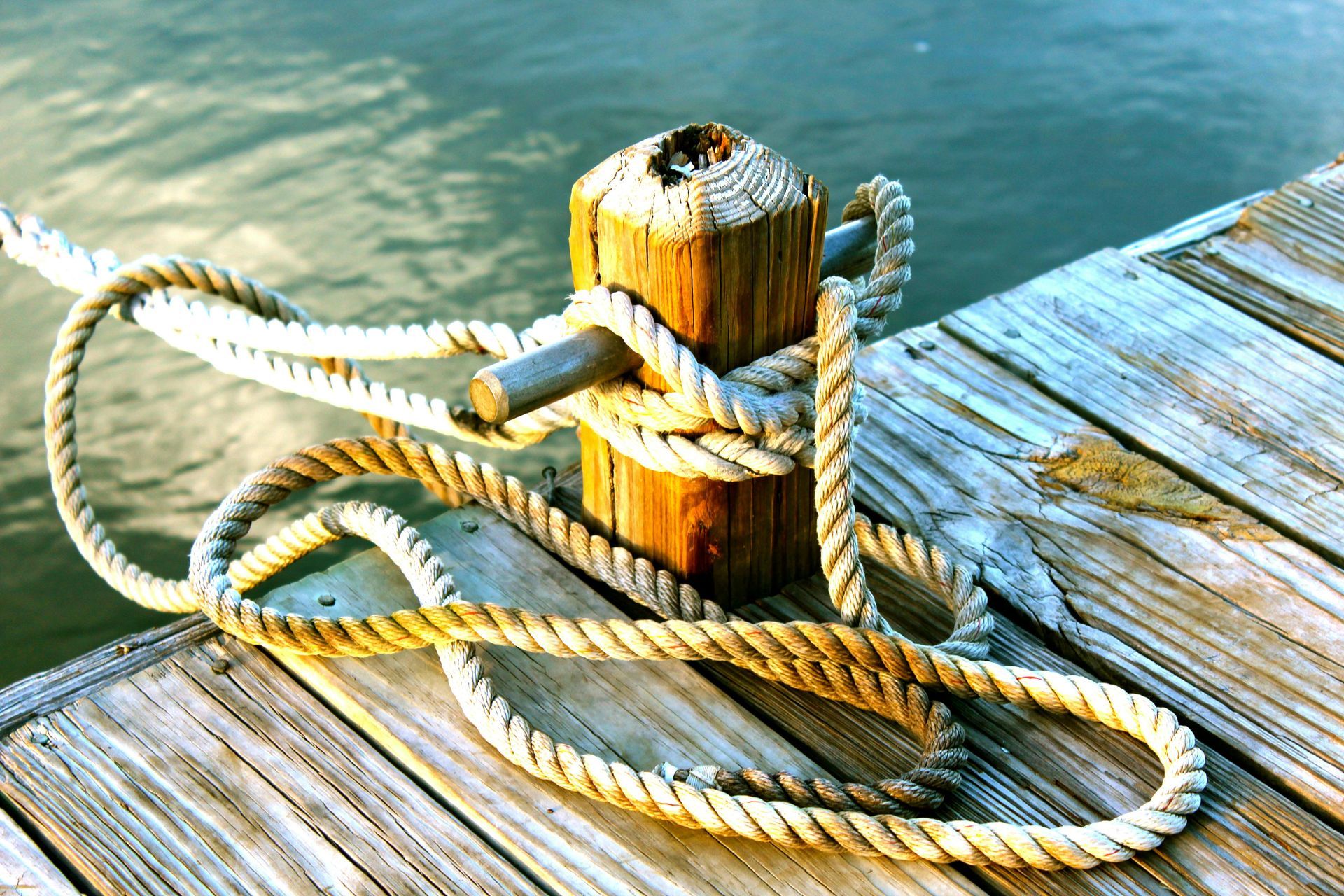 Wooden dock post with rope tied around it. Water in the background.