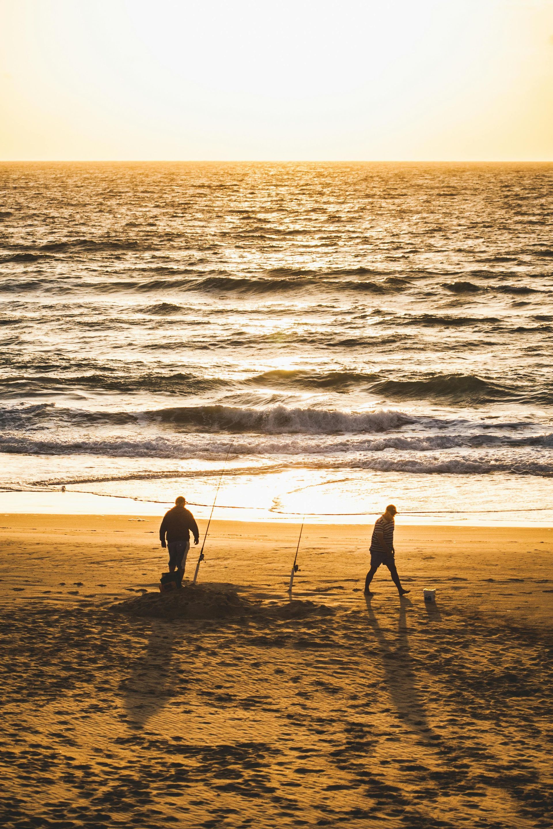 Two people walking on a beach at sunset, silhouetted against the ocean and golden sky.