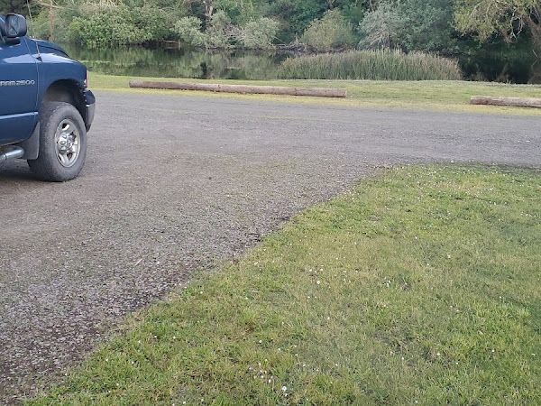 Blue truck parked on gravel next to a grassy area, with a body of water in the background.