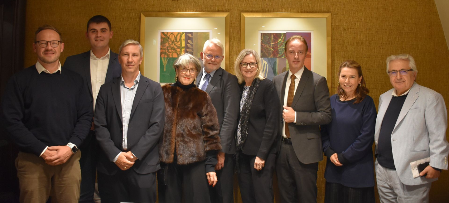 Eine Gruppe von Menschen steht in einem Raum zusammen, an dessen Wand gerahmte Kunstwerke hängen.