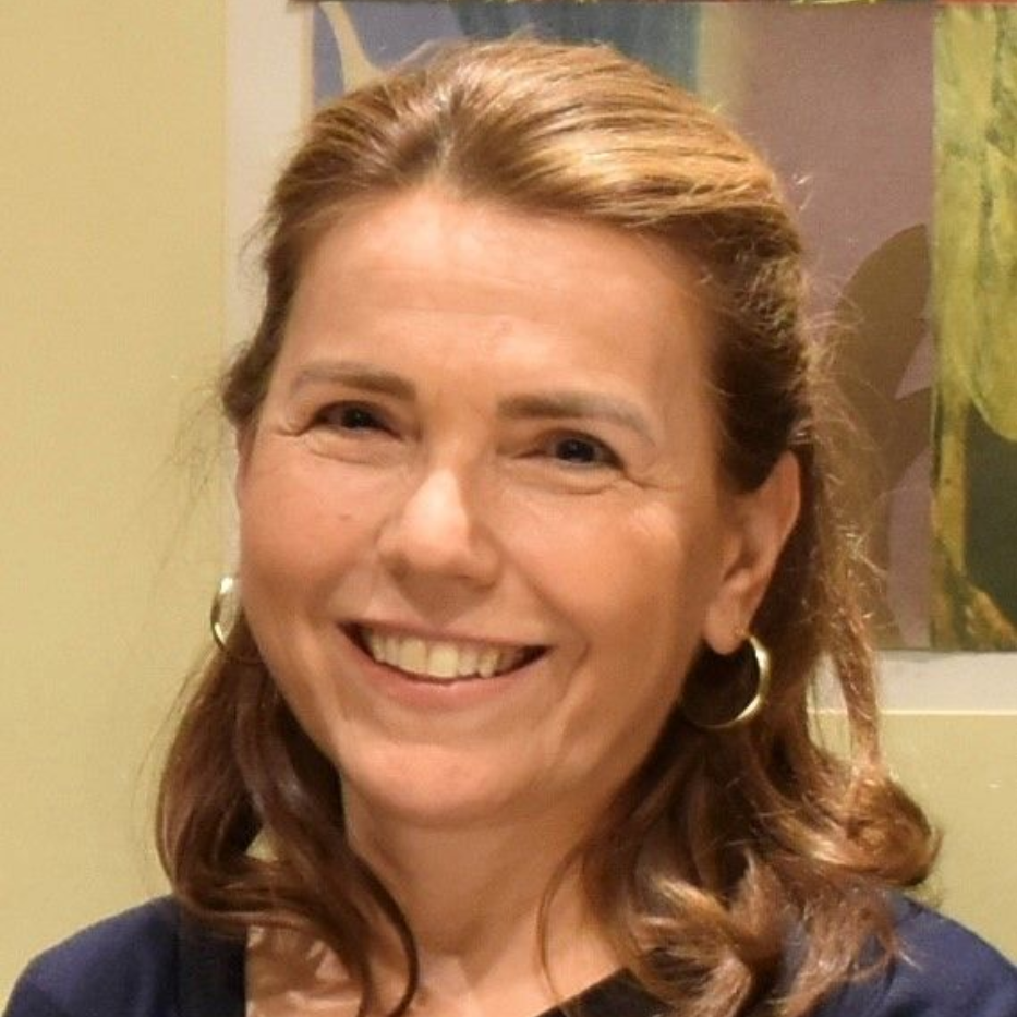 Eine Frau mit hellbraunem Haar lächelt in die Kamera und trägt goldene Creolen.