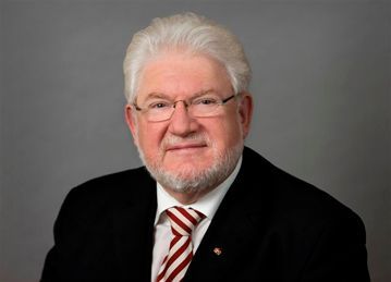 Mann mit Brille und Anzug, lächelnd, mit weißem Haar und Bart.