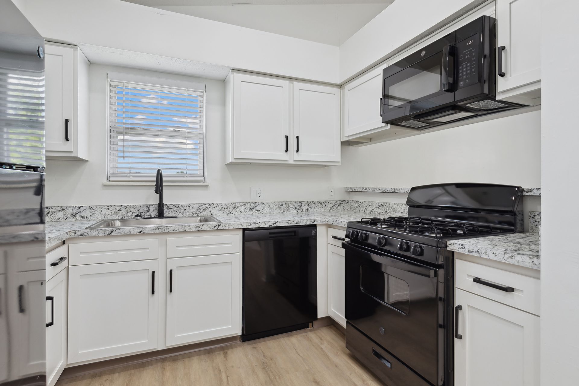 Aspire apartment kitchen with white cabinets, a black stove, a black microwave, and a sink.