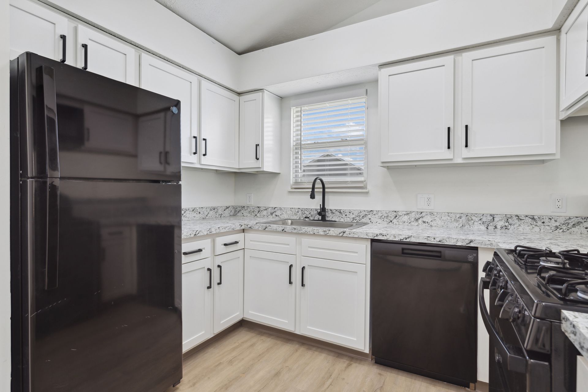 A kitchen with white cabinets , black appliances and a black refrigerator.