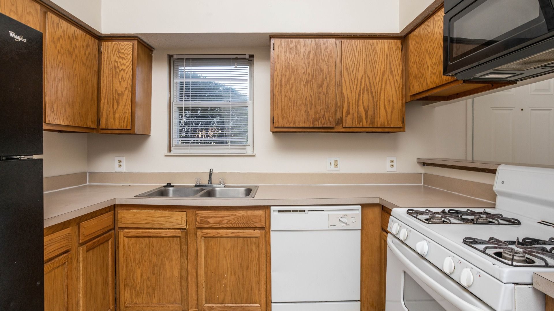 A kitchen with wooden cabinets , a stove , dishwasher , refrigerator and microwave.