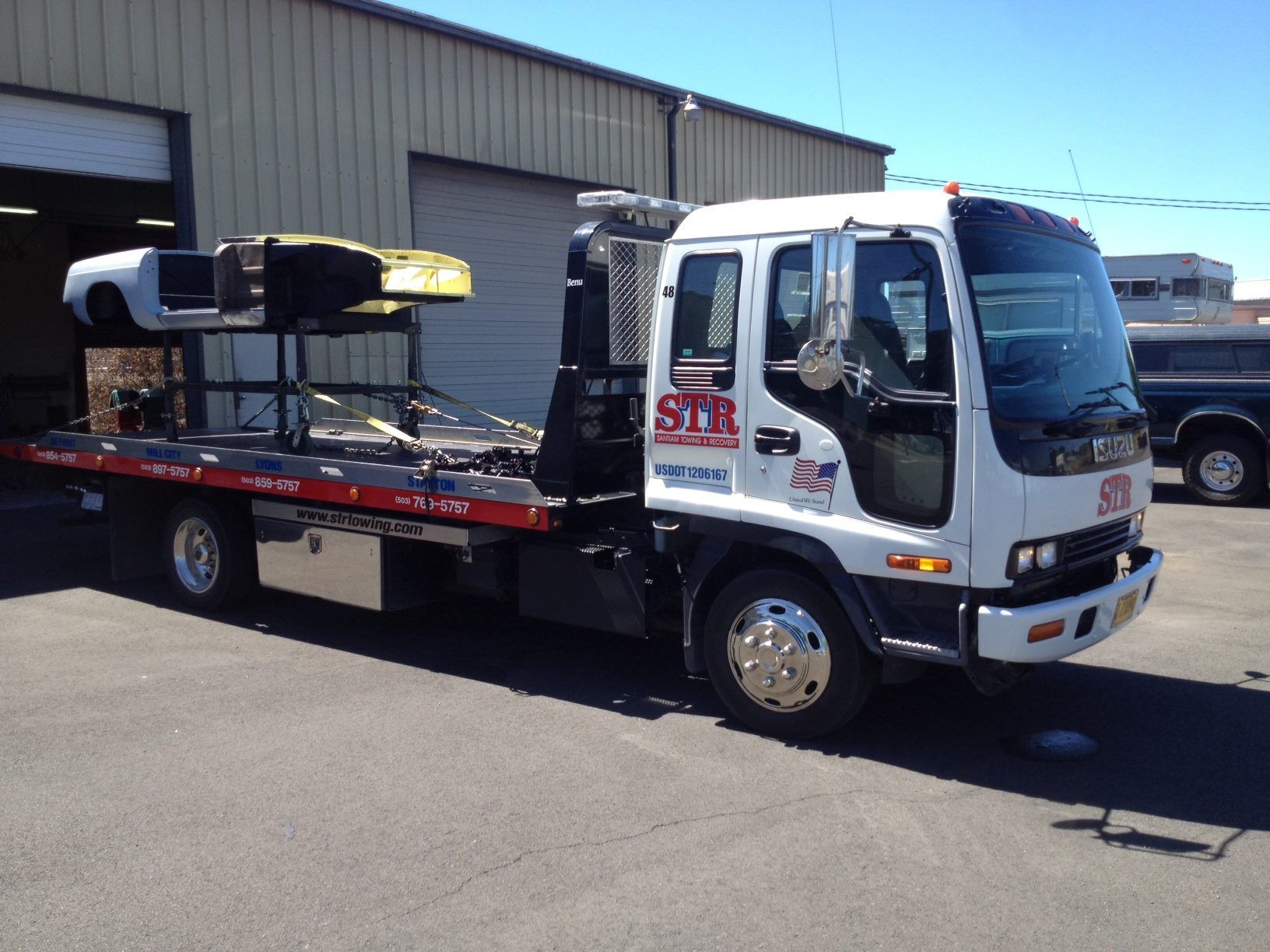 Tow truck with a white cab and flatbed parked outside an industrial building.