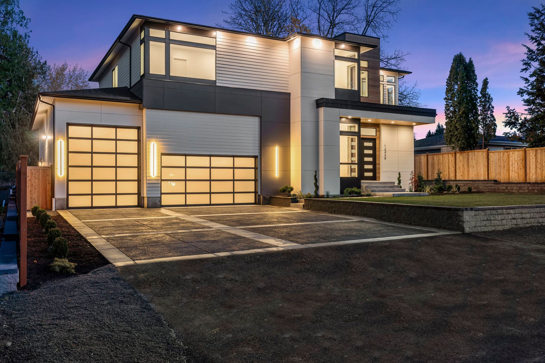 A modern house with a large garage door is lit up at night.
