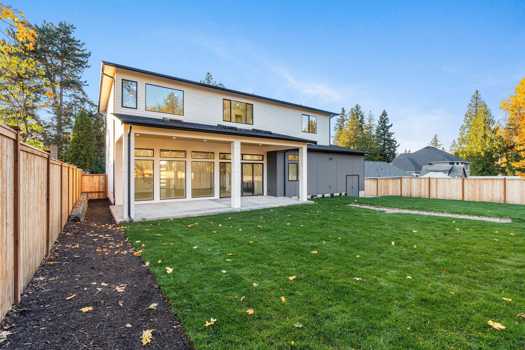 The backyard of a house with a large lawn and a wooden fence.