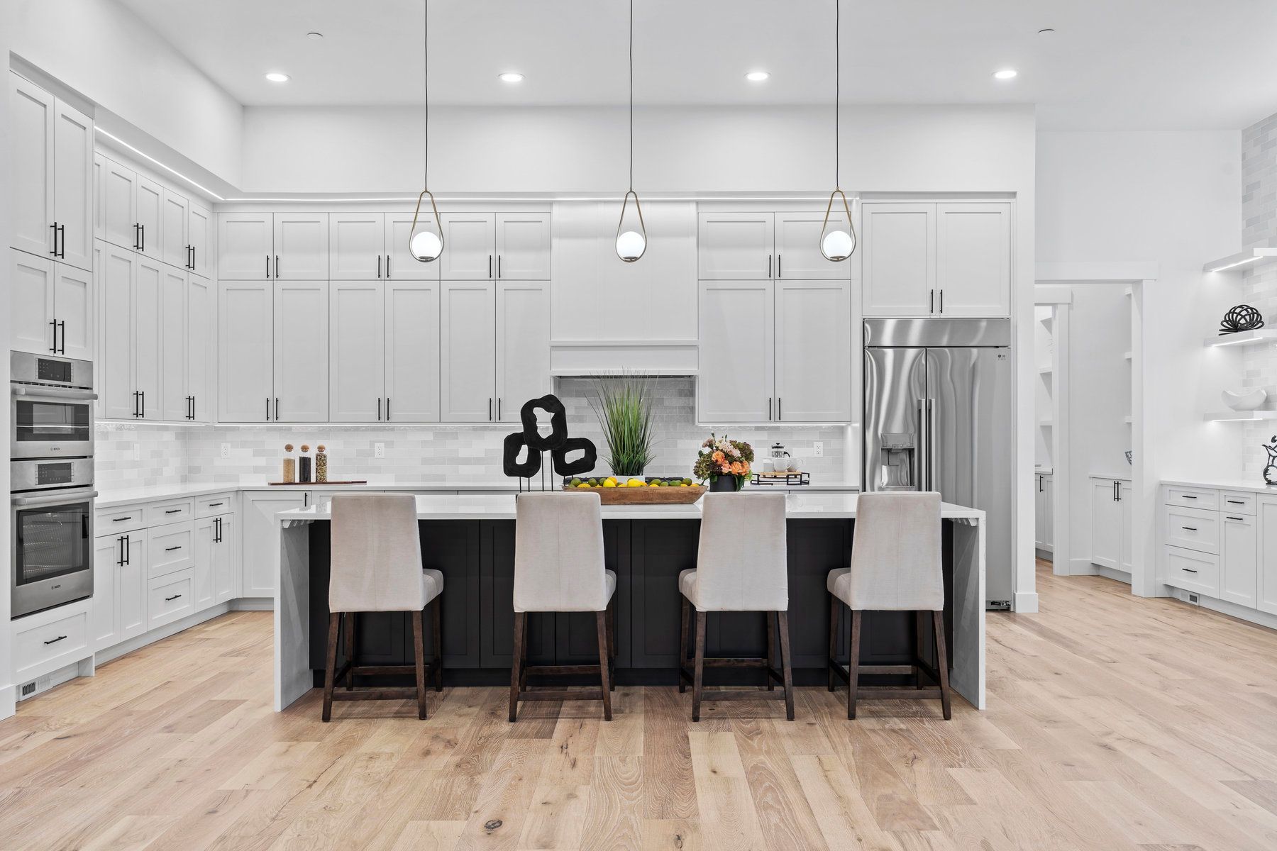A kitchen with white cabinets , stainless steel appliances , hardwood floors and a large island.