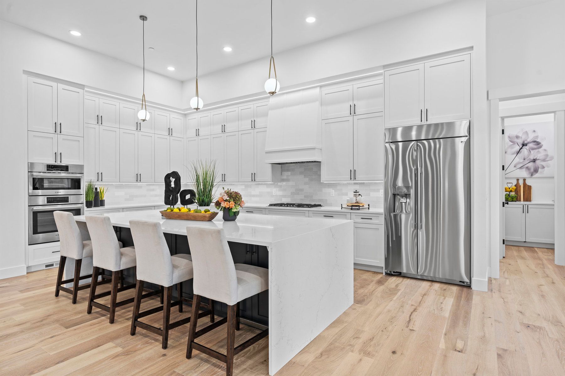 A kitchen with white cabinets , stainless steel appliances , hardwood floors and a large island.